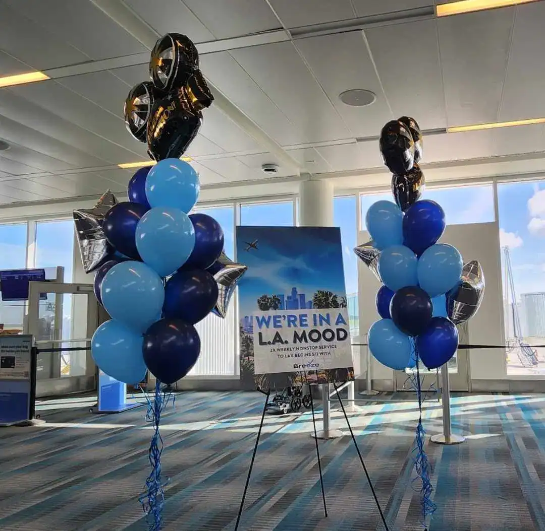 Blue Balloons in the gate area at CHS promoting a new route launch with a poster that reads "We're in a L.A. Mood 2x weekly nonstop service to LAX begins 5/2 with Breeze"